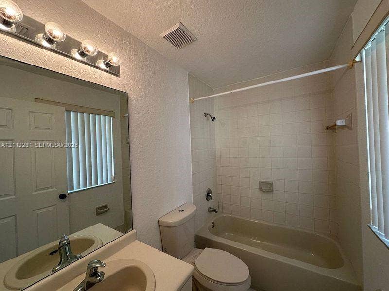 2615 SE 15th Place, #190, Homestead, FL 33035 Bathroom featuring a vanity with an integrated sink, wall-mounted four-bulb lighting fixture, full-width mirror, and a tile-surround bathtub