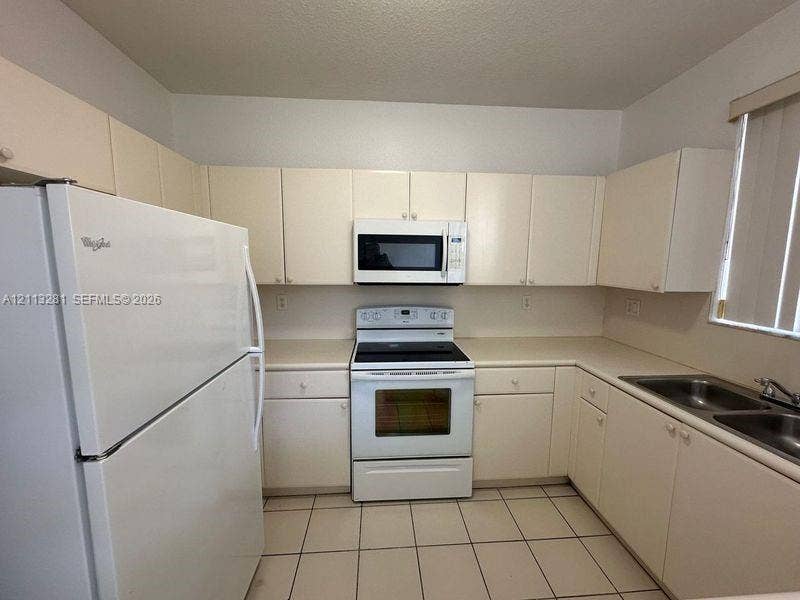 2615 SE 15th Place, #190, Homestead, FL 33035 Kitchen featuring off-white cabinetry, solid-surface countertops, tile flooring, and a white appliance suite including a built-in microwave and range