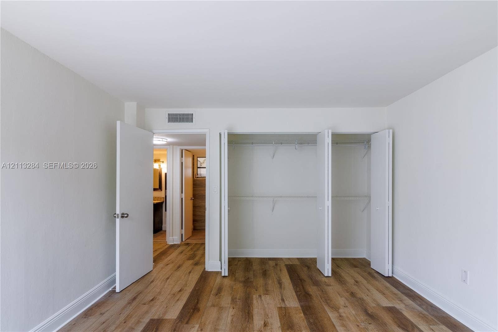 Room featuring wood-finish flooring, neutral wall paint, and a built-in closet with multi-panel doors and integrated shelving