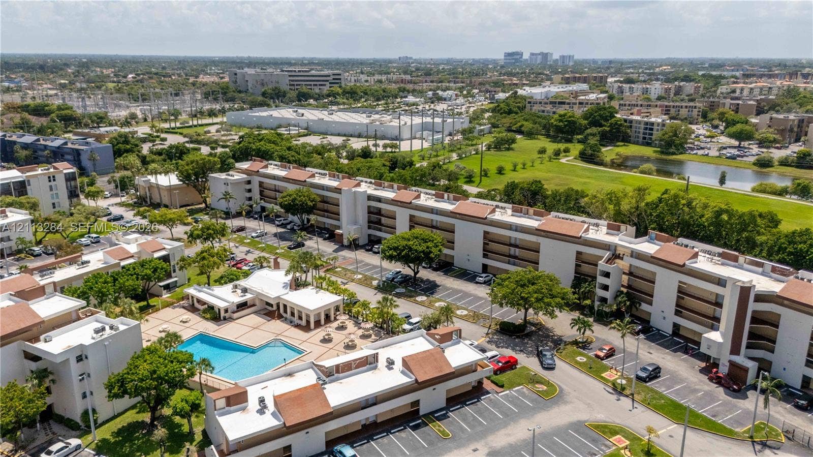 Aerial perspective of a multi-story residential complex featuring a swimming pool, paved pool deck, assigned surface parking, and mature palm landscaping