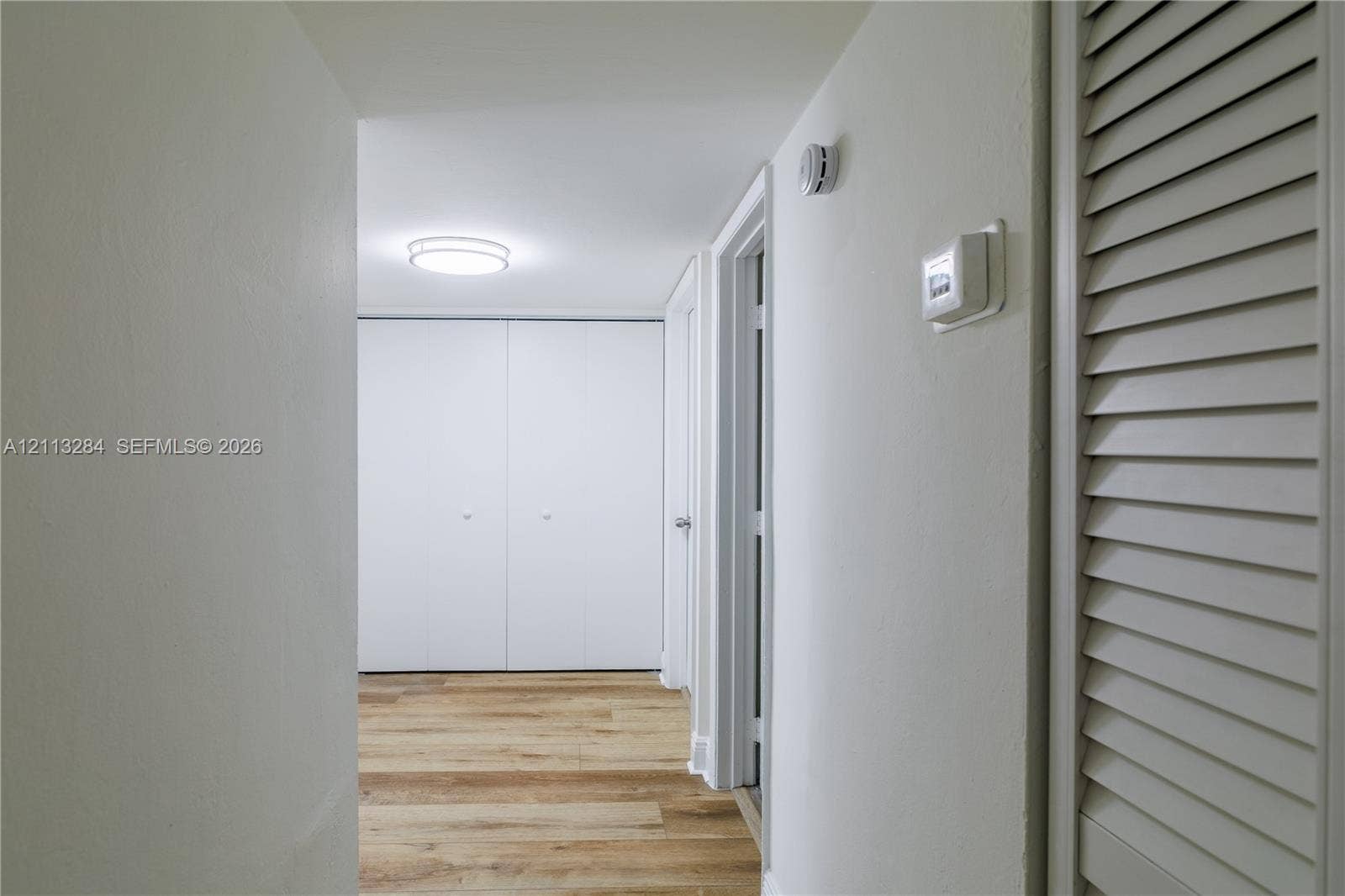 Hallway featuring wood-finish flooring, dual-door built-in closet, louvered closet door, and a flush-mount circular ceiling light