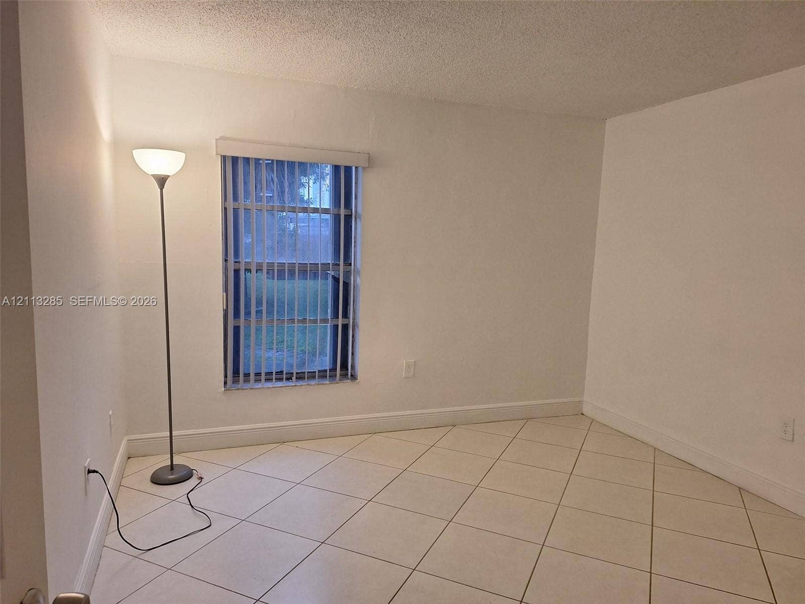 Interior room featuring neutral wall-to-wall ceramic tile flooring set on a diagonal pattern and a single window with vertical blinds