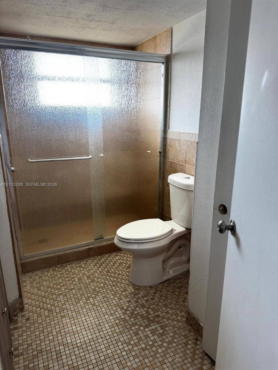 Bathroom featuring a glass-enclosed shower, mosaic tile flooring, and neutral wall tile surround