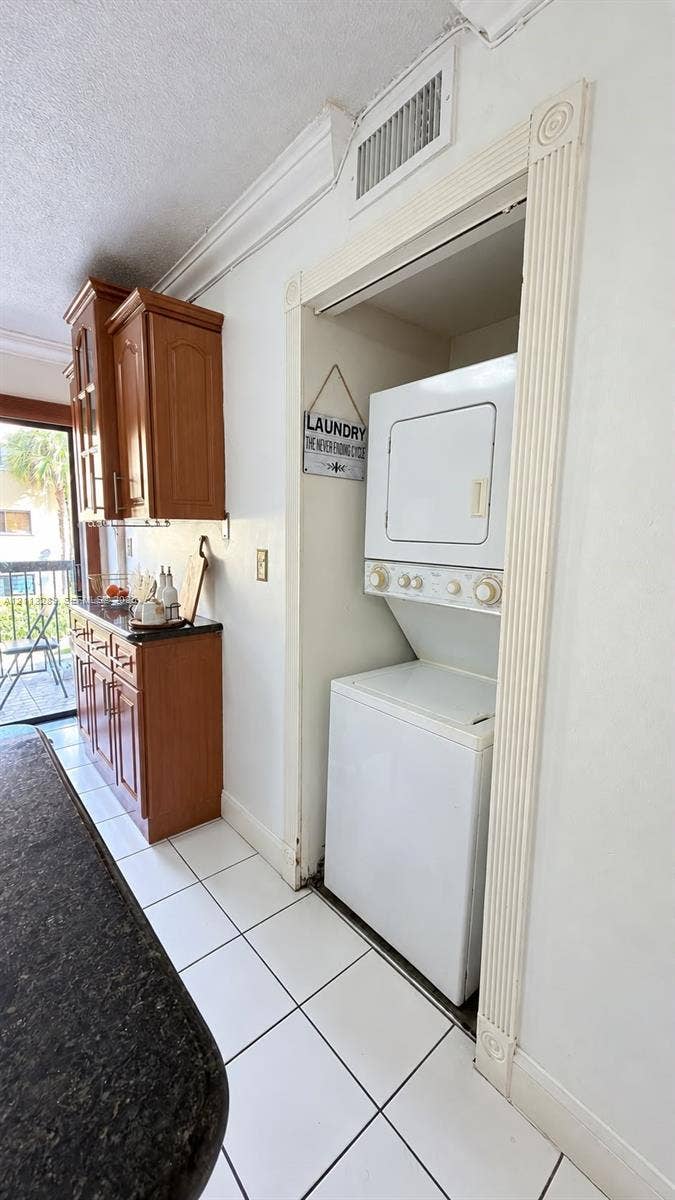 5460 W 21st Court, #208, Hialeah, FL 33016 Stacked washer and dryer unit, wood cabinetry with stone-finish countertops, and white tile flooring