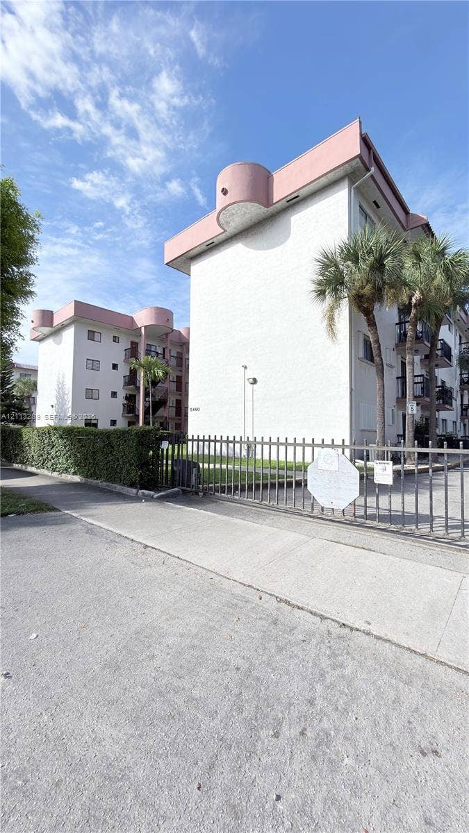 5460 W 21st Court, #208, Hialeah, FL 33016 Multi-story residential buildings featuring white stucco facades, decorative roofline architectural accents, tiered balcony railings, and a secure metal perimeter gate