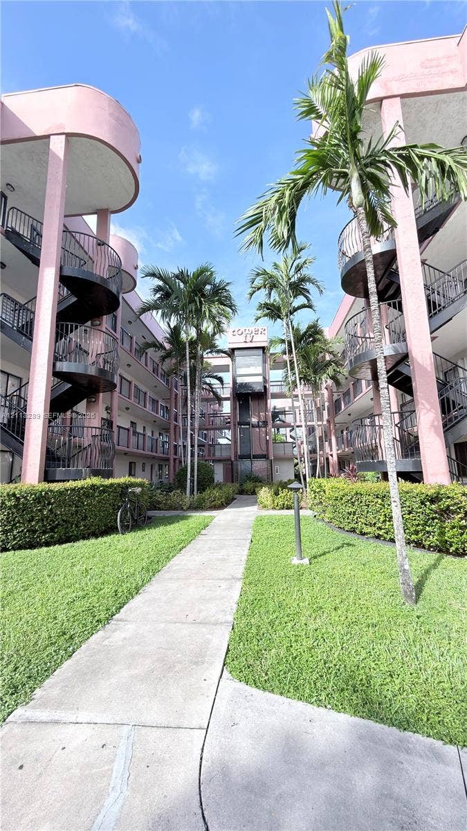 5460 W 21st Court, #208, Hialeah, FL 33016 Multi-story residential complex featuring curved architectural elements, wrought iron spiral staircases, central concrete walkway, mature palm trees, and manicured landscaping