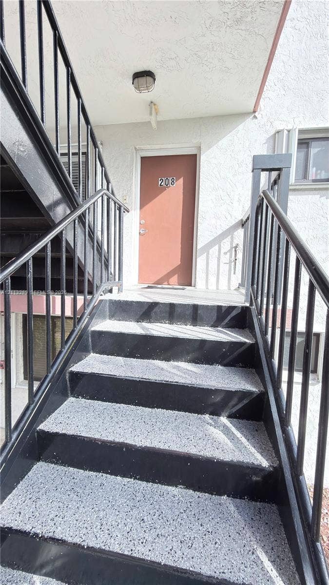 5460 W 21st Court, #208, Hialeah, FL 33016 Exterior staircase featuring black metal railings and concrete-finish treads with a textured surface, leading to an elevated landing with a covered entryway and ceiling-mounted light fixture