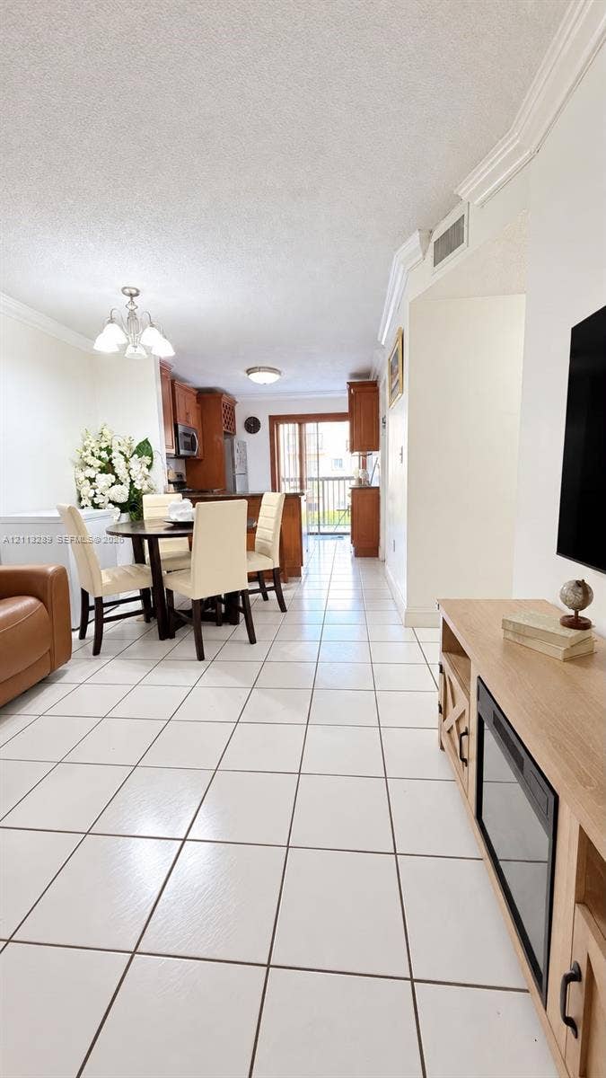 5460 W 21st Court, #208, Hialeah, FL 33016 Open-concept interior featuring uniform white tile flooring, crown molding, wood-finish cabinetry, and glass sliding doors providing exterior access