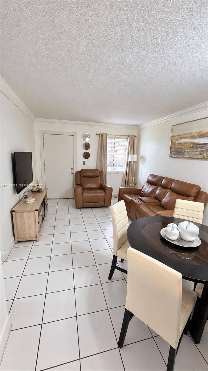 5460 W 21st Court, #208, Hialeah, FL 33016 Living area featuring white ceramic tile flooring, crown molding, and natural light from a single-pane window