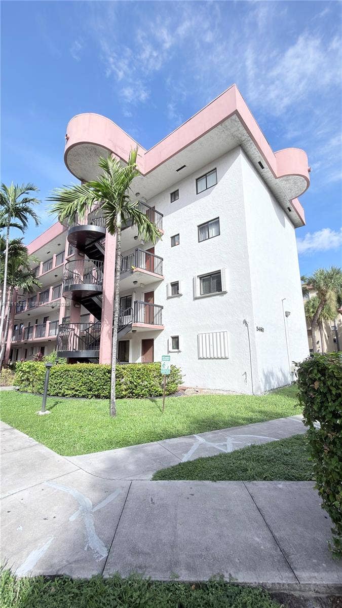 5460 W 21st Court, #208, Hialeah, FL 33016 Multi-story residential building featuring textured stucco exterior walls, prominent spiral metal staircases, recessed balconies with metal railings, and integrated palm tree landscaping