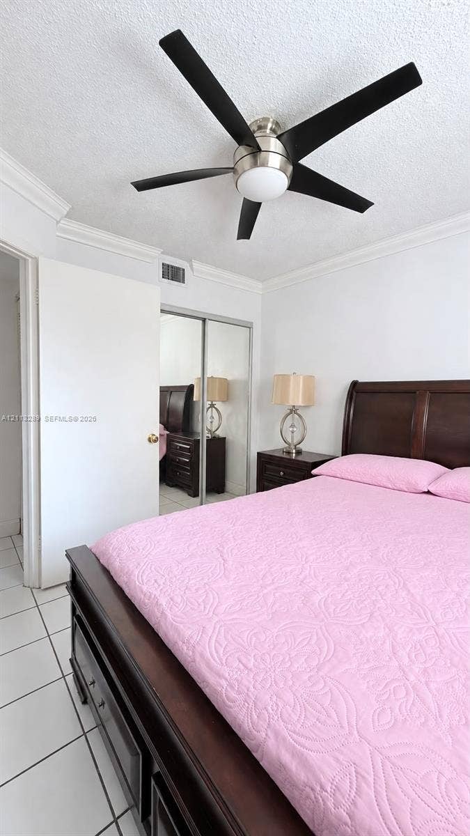 5460 W 21st Court, #208, Hialeah, FL 33016 Room featuring white ceramic tile flooring, crown molding, a brushed nickel and black ceiling fan with integrated lighting, and a closet with mirrored sliding doors
