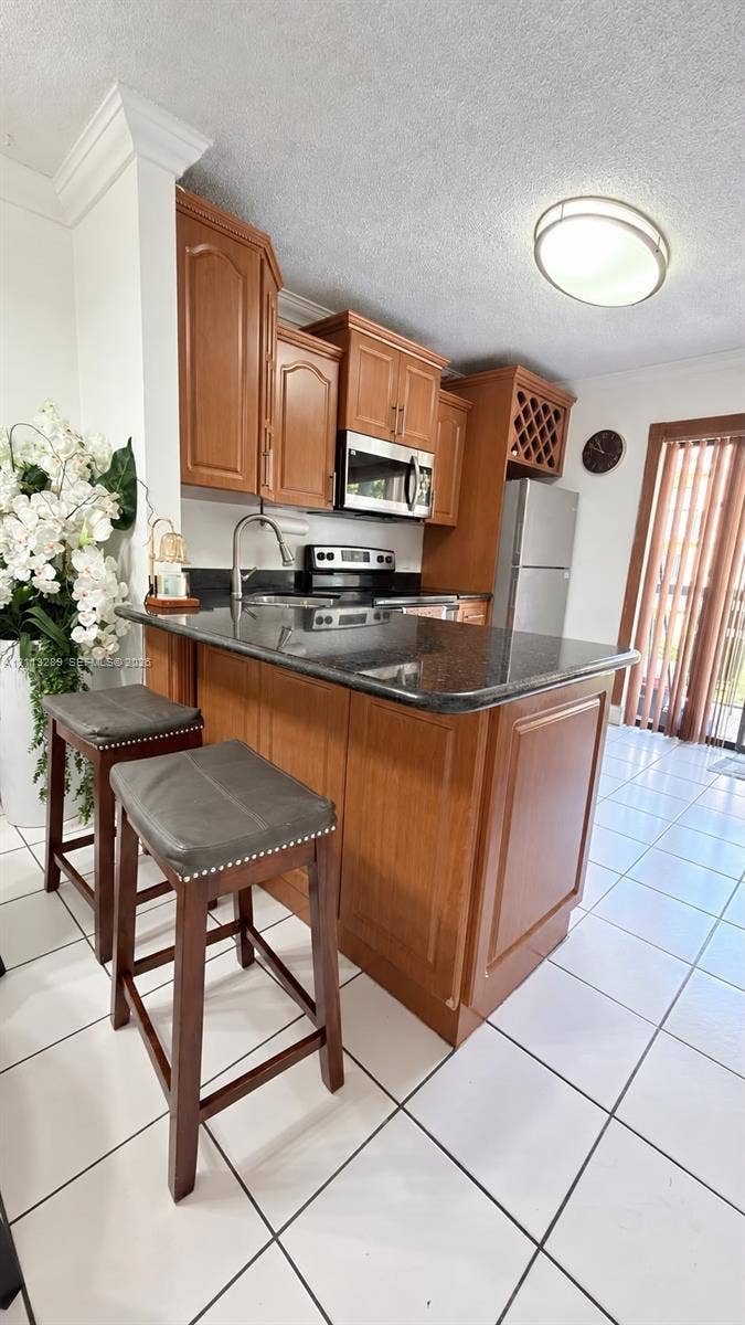 5460 W 21st Court, #208, Hialeah, FL 33016 Kitchen featuring wood cabinetry, stone countertops, stainless steel appliances, built-in wine rack, and tile flooring