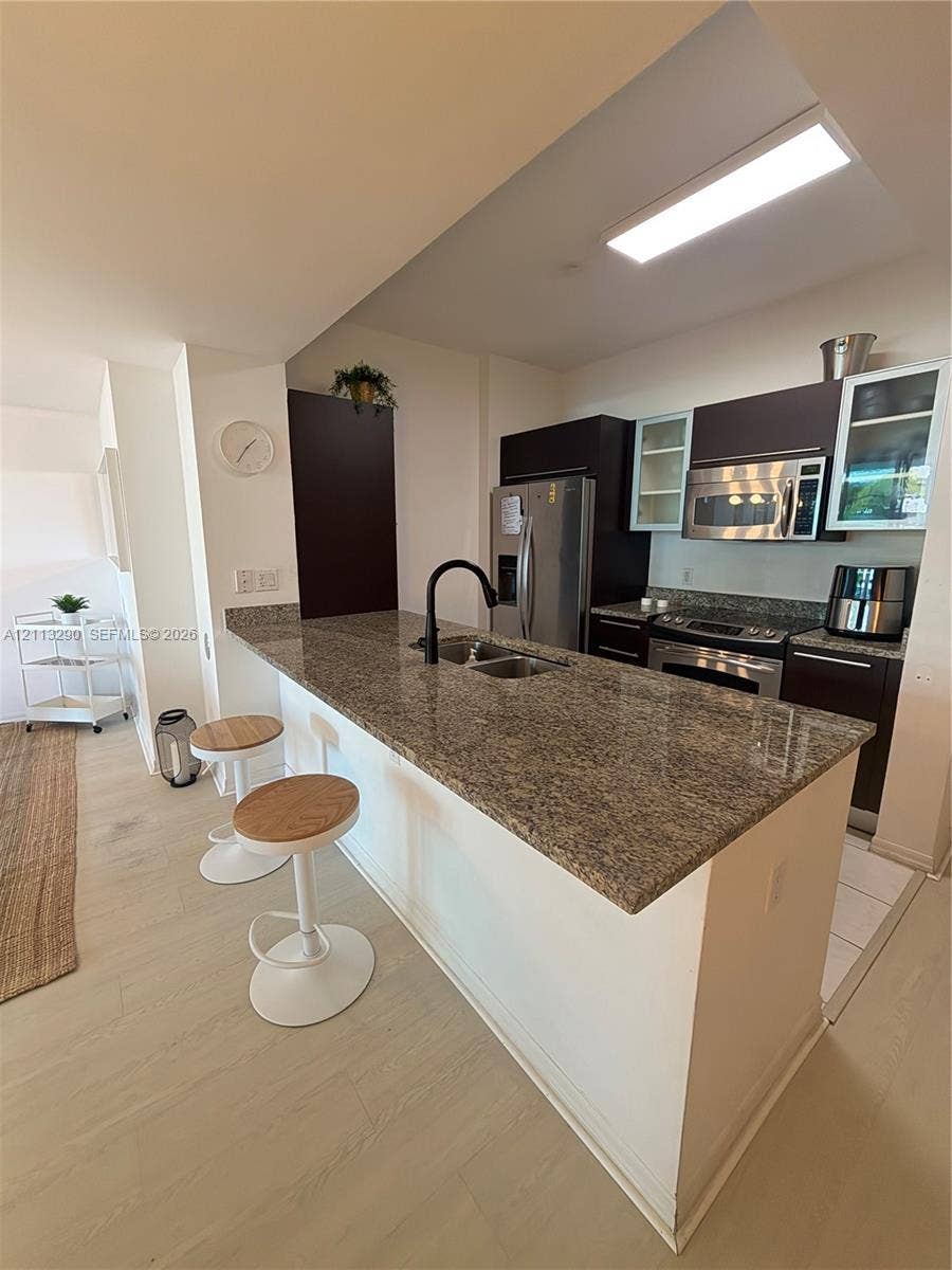 951 Brickell Avenue, #405, Miami, Miami, FL 33131 Kitchen featuring a peninsula with stone-finish countertops, stainless steel appliances, dark cabinetry, and a high-arc matte black faucet