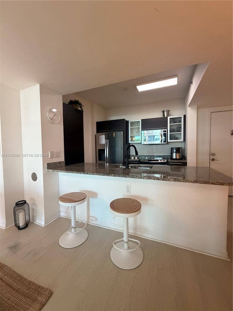951 Brickell Avenue, #405, Miami, Miami, FL 33131 Kitchen featuring a stone-surface breakfast bar, dark cabinetry, stainless steel appliances, a gooseneck faucet, and light-tone wood-finish flooring