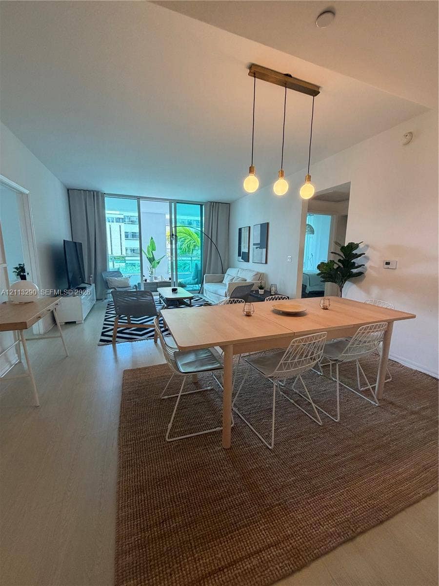 951 Brickell Avenue, #405, Miami, Miami, FL 33131 Open-concept living space featuring wood-finish flooring, floor-to-ceiling glass sliding doors, and a linear pendant light fixture with three exposed bulbs