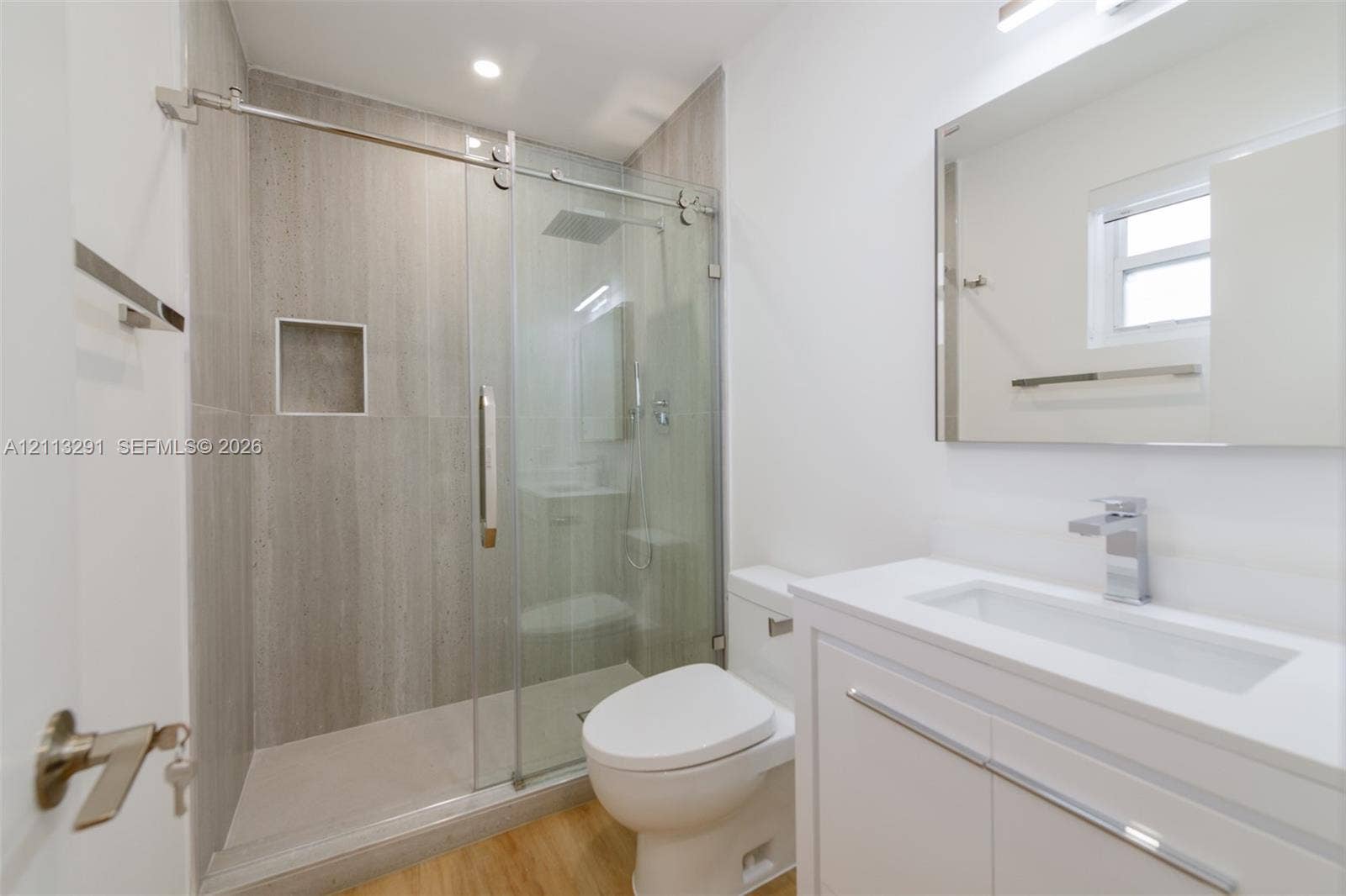 Bathroom featuring a glass-enclosed shower with floor-to-ceiling tile, built-in recessed niche, modern vanity with a white countertop, and wood-finish flooring