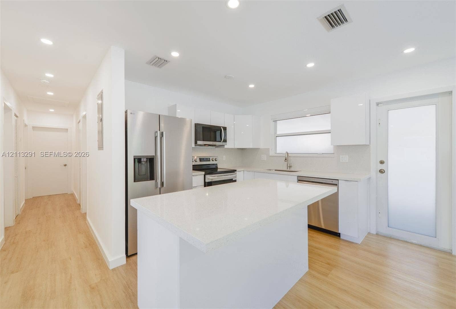Kitchen featuring white flat-panel cabinetry, a central island with a quartz countertop, stainless steel appliances, and wood-finish flooring