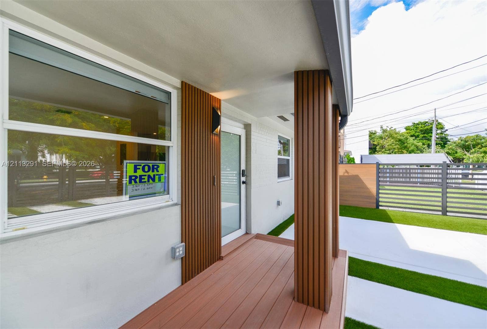 Covered entryway featuring wood-finish decking, vertical slat accents, a structural column, and a modern exterior light fixture