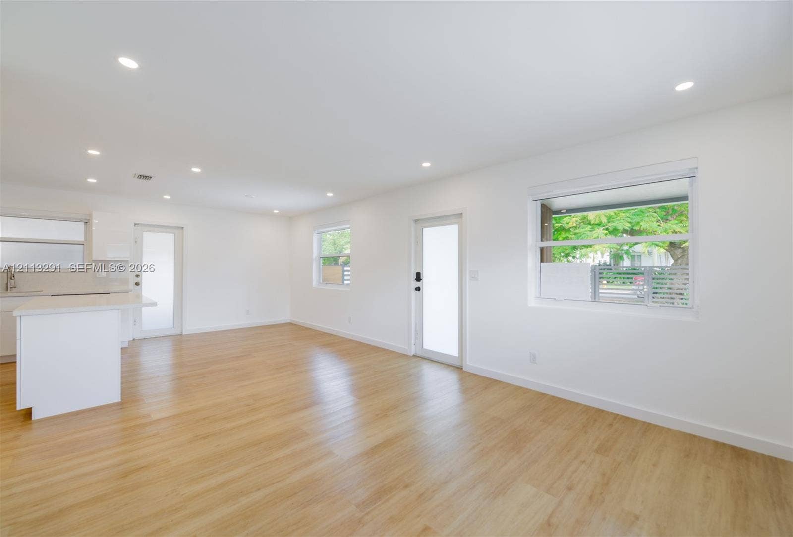 Open-concept space featuring recessed ceiling lighting, light-toned wood-finish flooring, white walls, and multiple windows with white frames