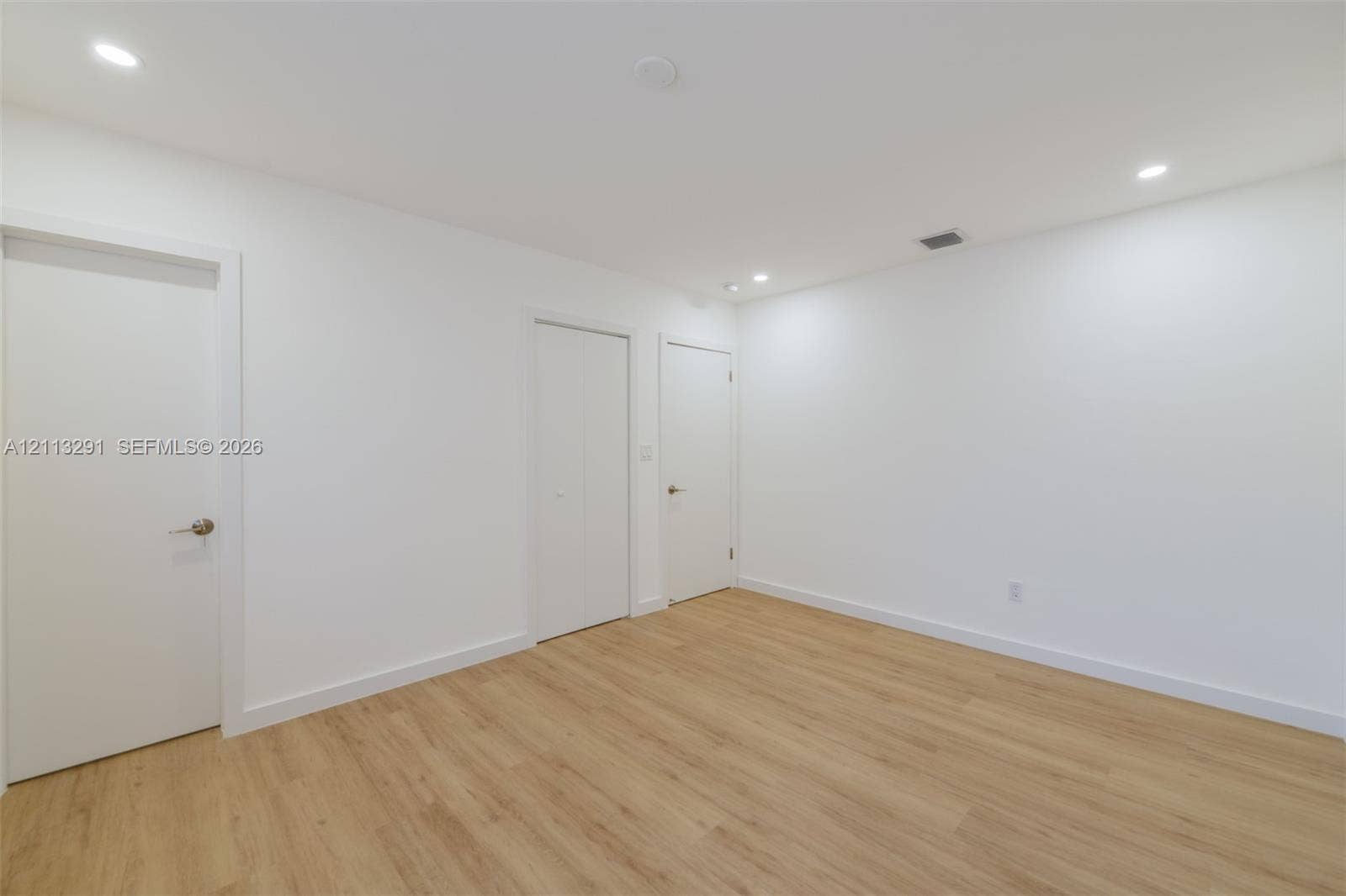 Interior room featuring wood-finish flooring, recessed lighting, and multiple interior doors with satin nickel hardware