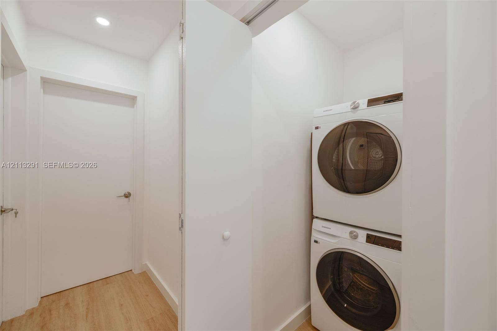 Stacked washer and dryer unit with wood-finish flooring and recessed lighting