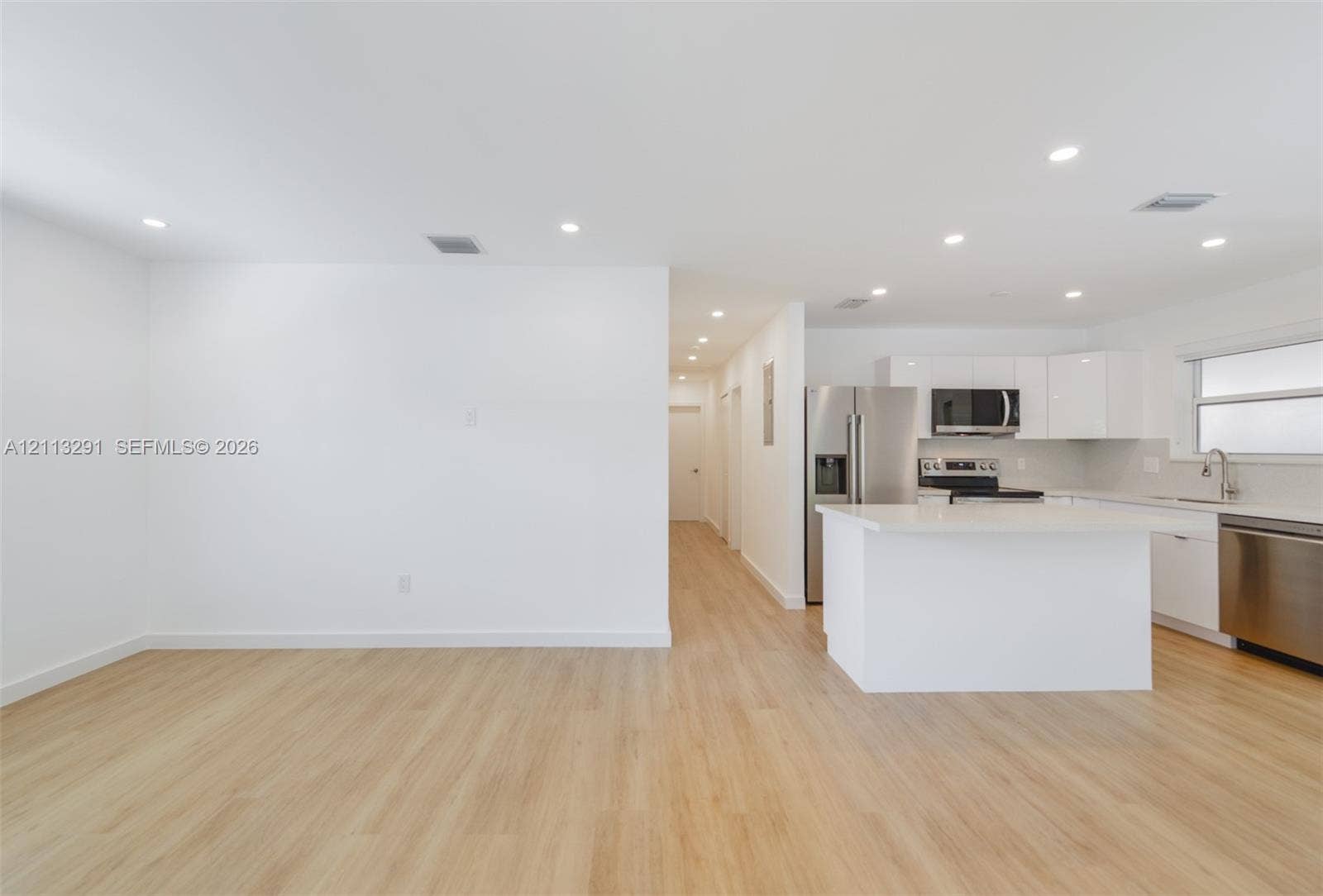 Open-concept interior featuring light wood-finish flooring, recessed lighting, white gloss cabinetry, quartz countertops, and stainless steel appliances