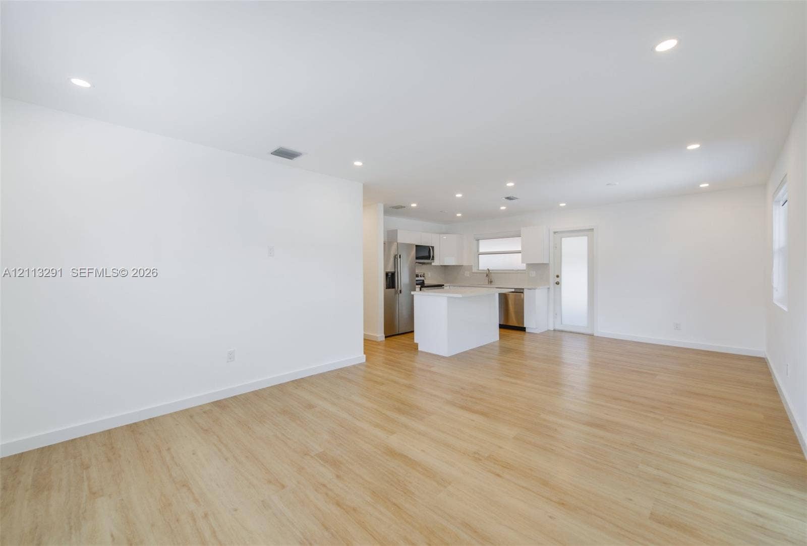 Open floor plan featuring wood-finish flooring, recessed lighting, white cabinetry, a center island, and stainless steel appliances