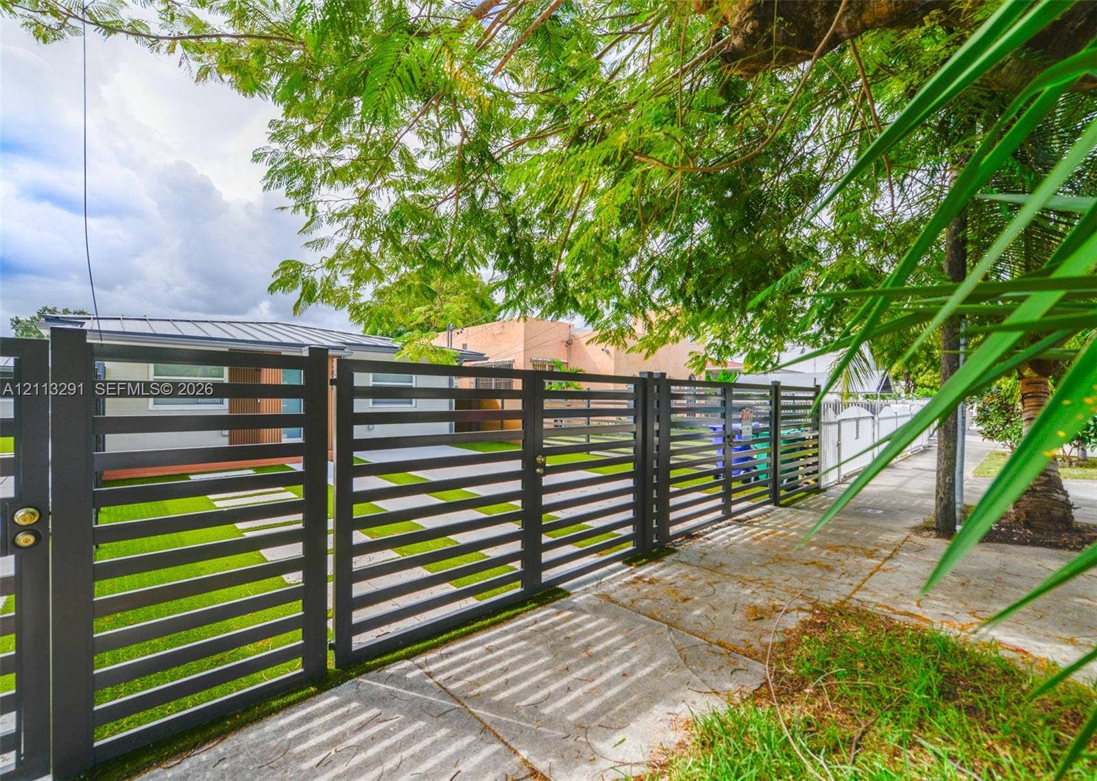 Horizontal slat metal fencing with integrated gate, artificial turf yard, and concrete paver driveway
