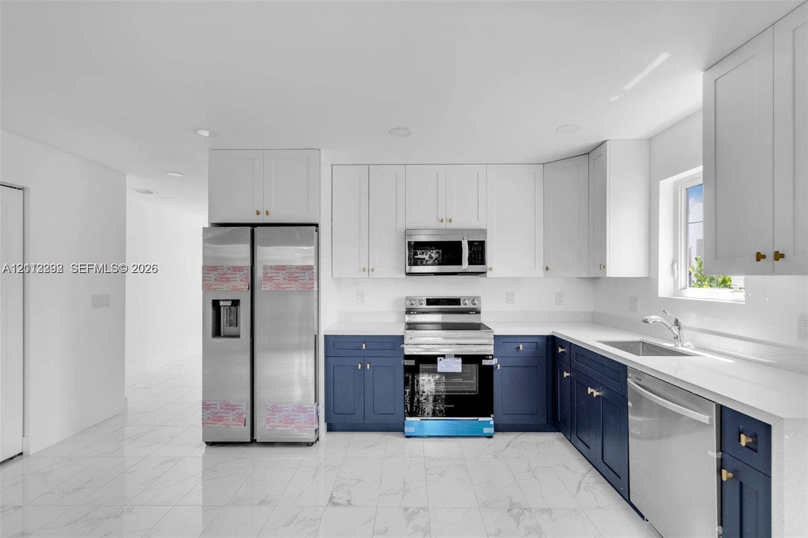 Kitchen featuring white upper cabinetry, navy blue lower cabinetry, light-toned stone-finish countertops, stainless steel appliances, and large-format tile flooring