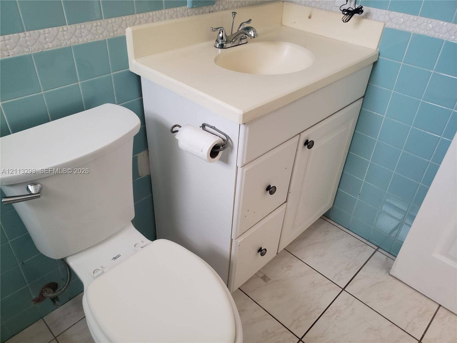 Bathroom featuring a white vanity with integrated basin, ceramic wall tiling, white floor tile, and a porcelain toilet