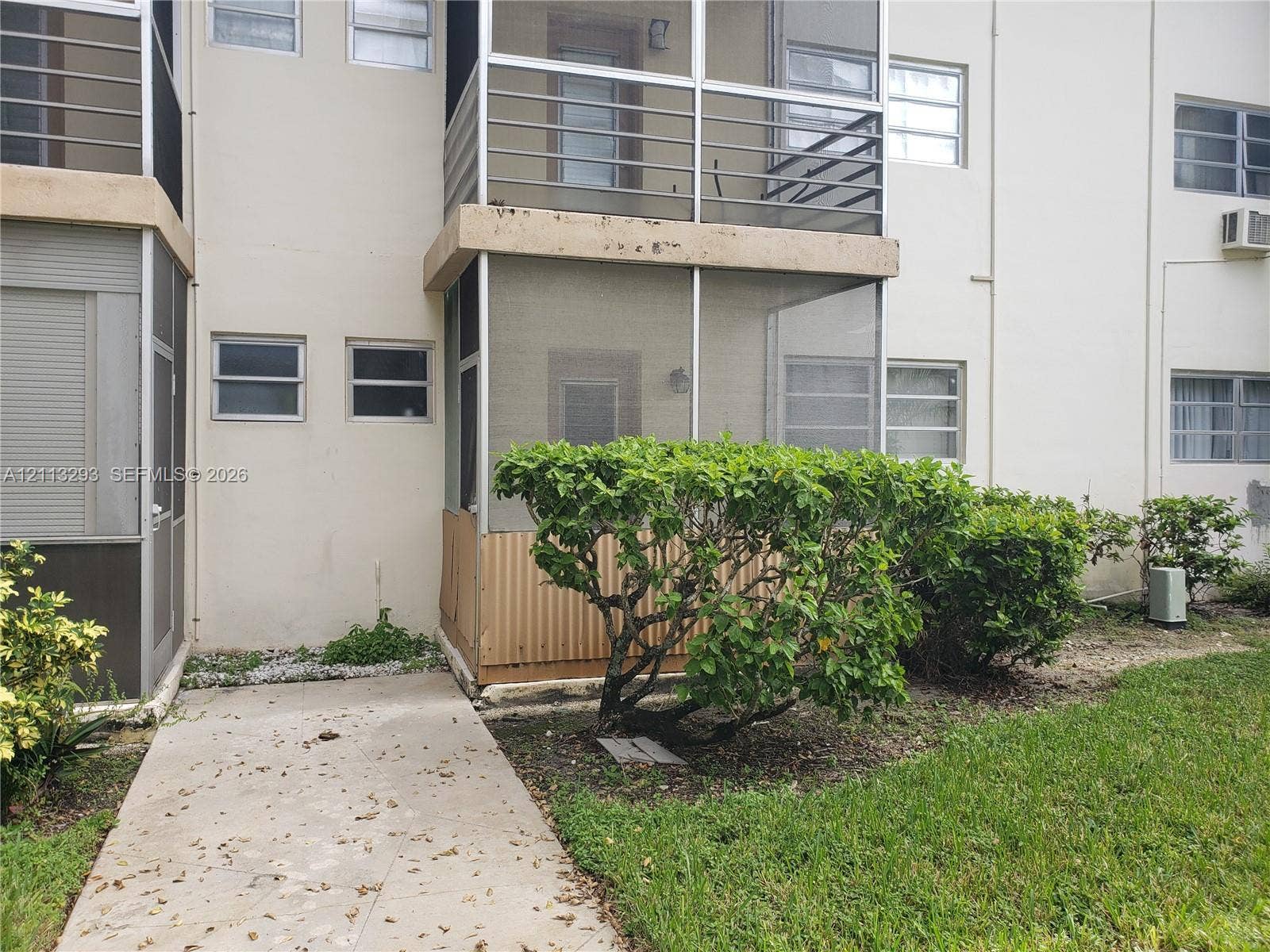 Exterior view featuring a concrete walkway, multi-level screened-in balconies, aluminum railing, and mature landscaping