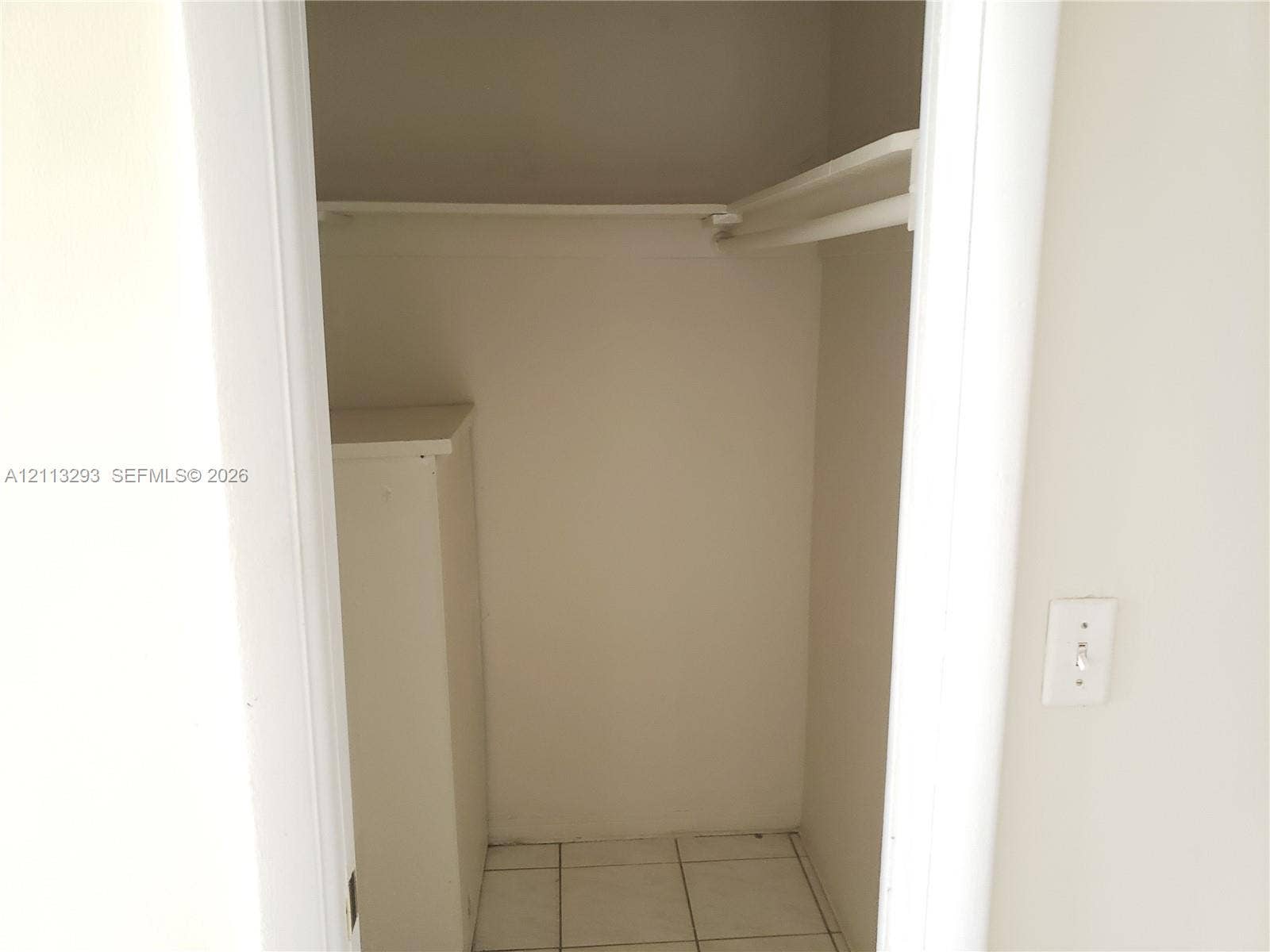 Storage closet featuring tile flooring, a built-in cabinet, and a structural hanging rod with upper shelf