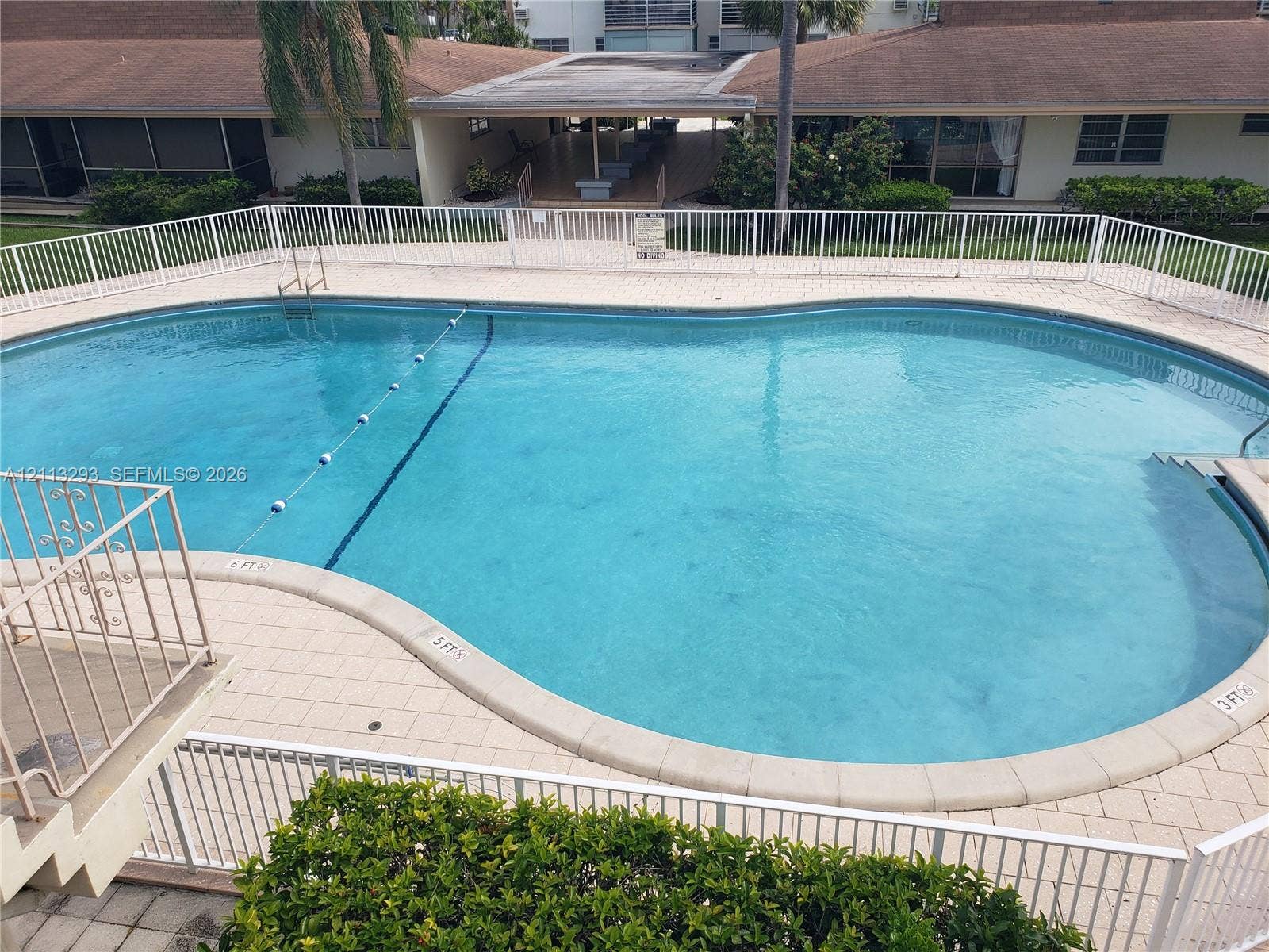 In-ground swimming pool featuring a curved concrete perimeter, tiled decking, and a white metal safety fence