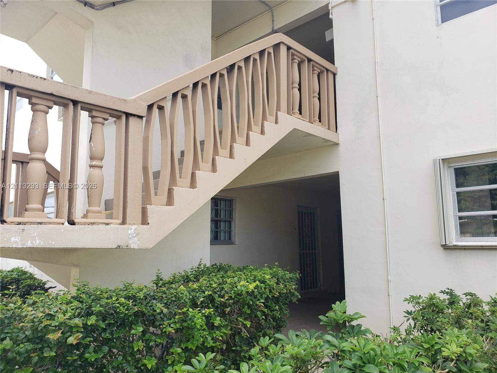 Exterior staircase featuring custom geometric concrete balusters, smooth stucco facade, and manicured shrubbery