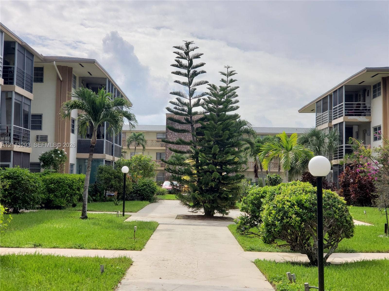 Landscaped courtyard featuring concrete walkways, manicured lawn, mature palm trees, and exterior post-mounted lighting
