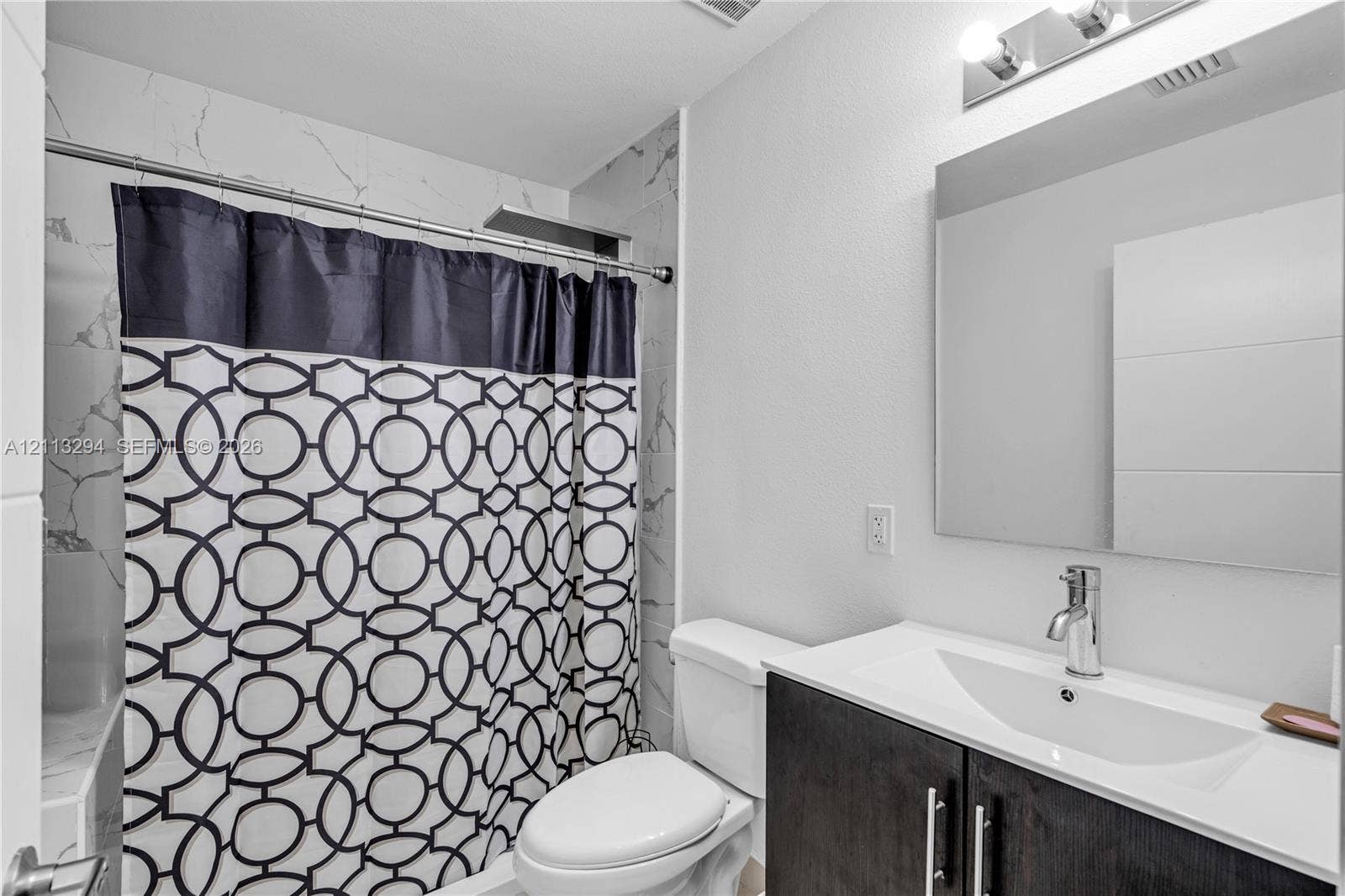 25880 SW 139th Path, #0, Homestead, FL 33032 Bathroom featuring a dark-finish vanity with a rectangular sink, stone-pattern wall tile surround in the shower, polished chrome faucet, and a wall-mounted mirror with overhead lighting