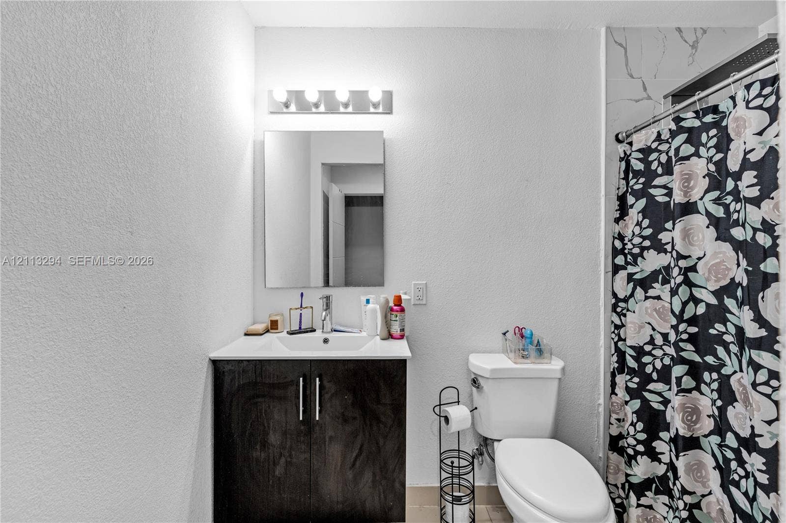 25880 SW 139th Path, #0, Homestead, FL 33032 Bathroom featuring a vanity with dark wood-finish cabinetry, a white integrated sink, a rectangular wall-mounted mirror, a four-bulb light fixture, and a tiled shower surround