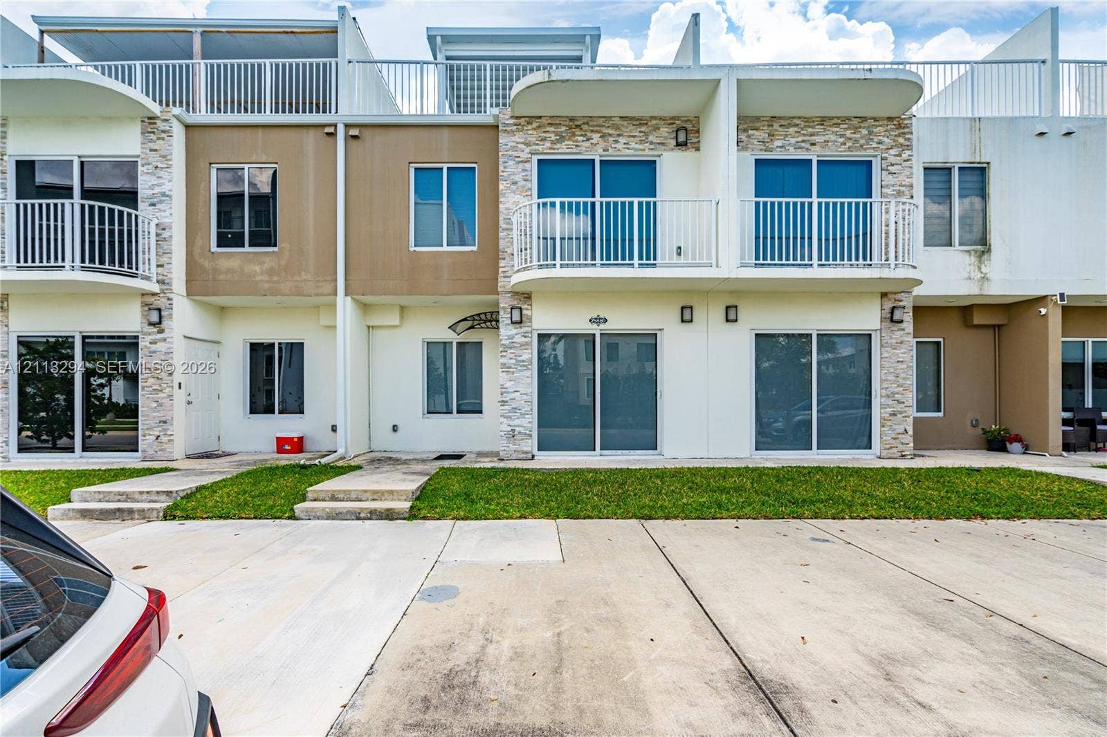 25880 SW 139th Path, #0, Homestead, FL 33032 Multi-level exterior facade featuring stone veneer detailing, metal balcony railings, sliding glass door entryways, and concrete paved parking