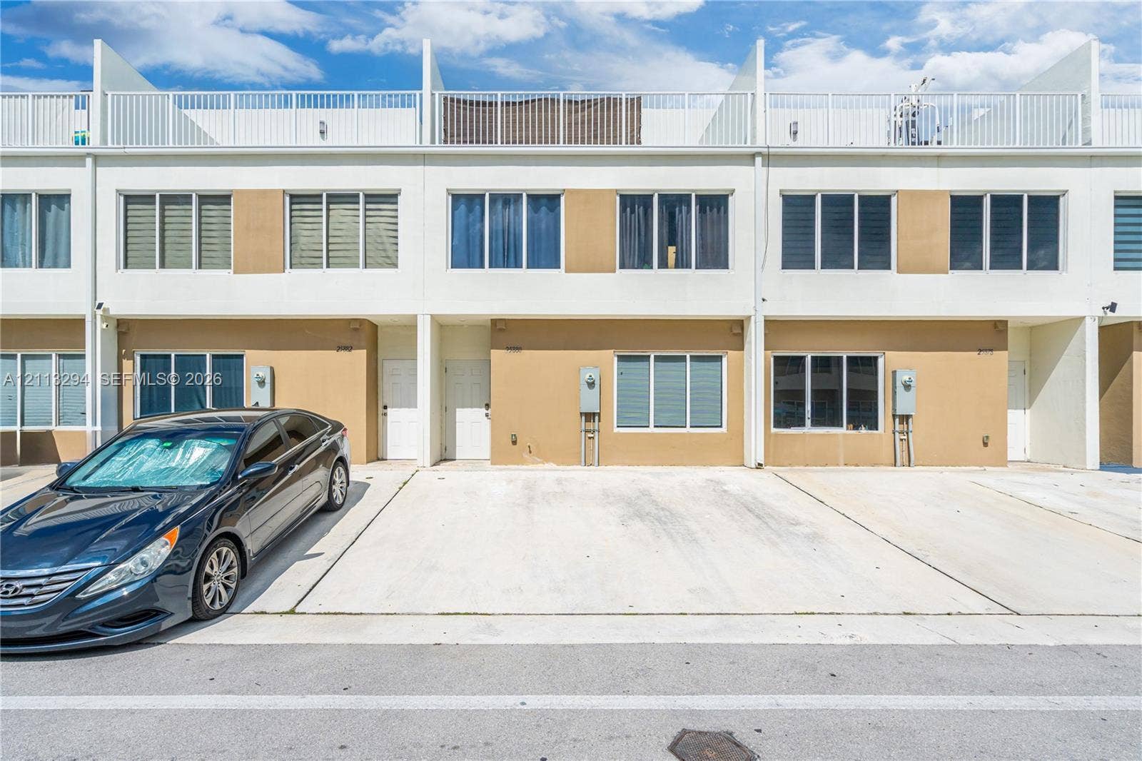 25880 SW 139th Path, #0, Homestead, FL 33032 Multi-level townhome exterior featuring a smooth stucco facade, concrete driveway, and a top-level rooftop terrace with metal railings