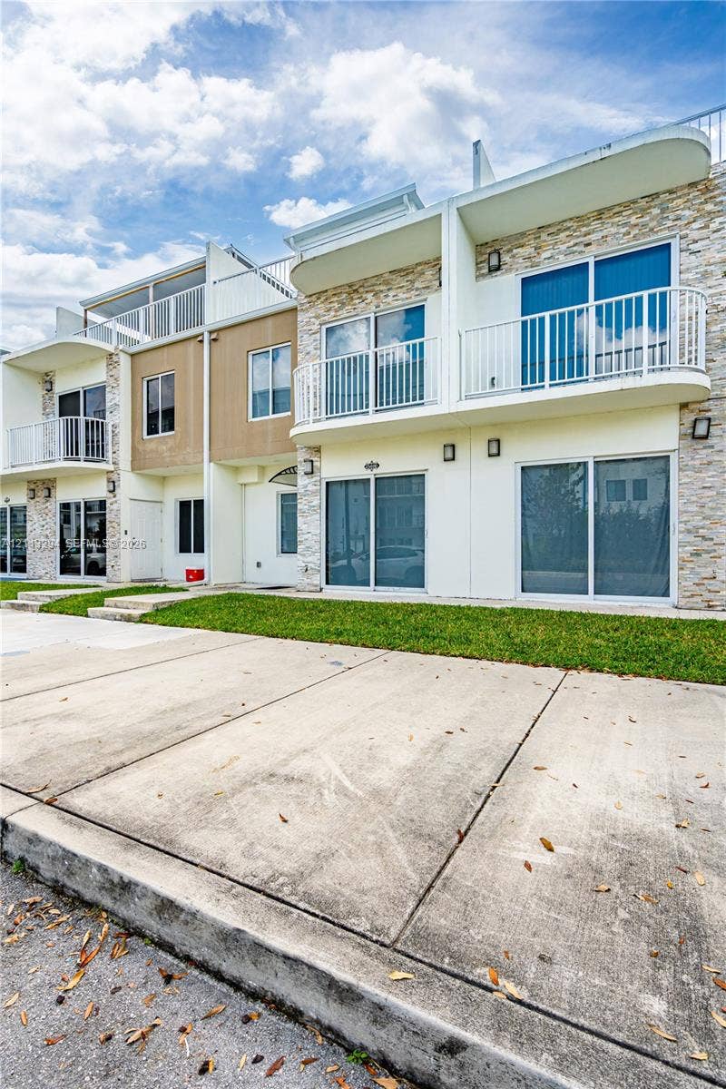 25880 SW 139th Path, #0, Homestead, FL 33032 Multi-level exterior featuring stacked stone accents, smooth-finish siding, private balconies with white railings, and sliding glass doors