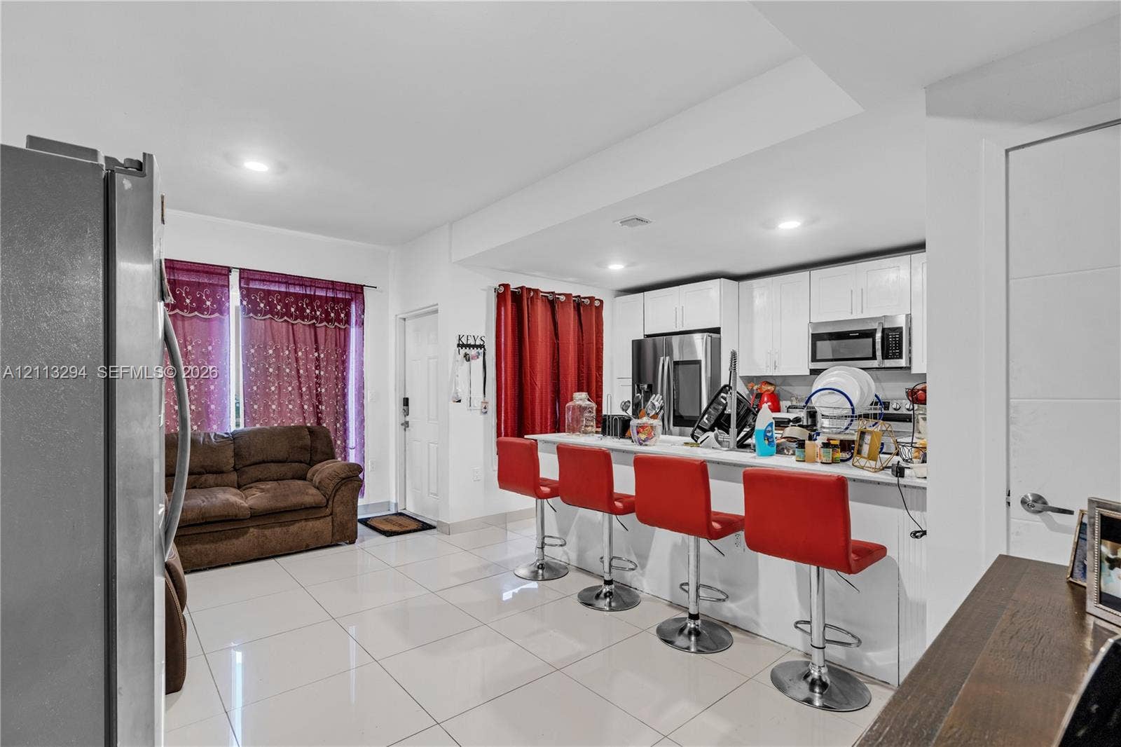 25880 SW 139th Path, #0, Homestead, FL 33032 Open-concept kitchen featuring high-gloss white cabinetry, polished tile flooring, stainless steel appliances, and a breakfast bar