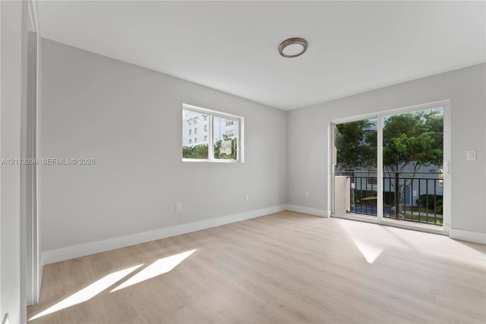1101 NE 80th Street, #302, Miami, Miami, FL 33138 Neutral-toned interior featuring wood-finish flooring, a flush-mount light fixture, and sliding glass doors opening to a balcony with metal railing