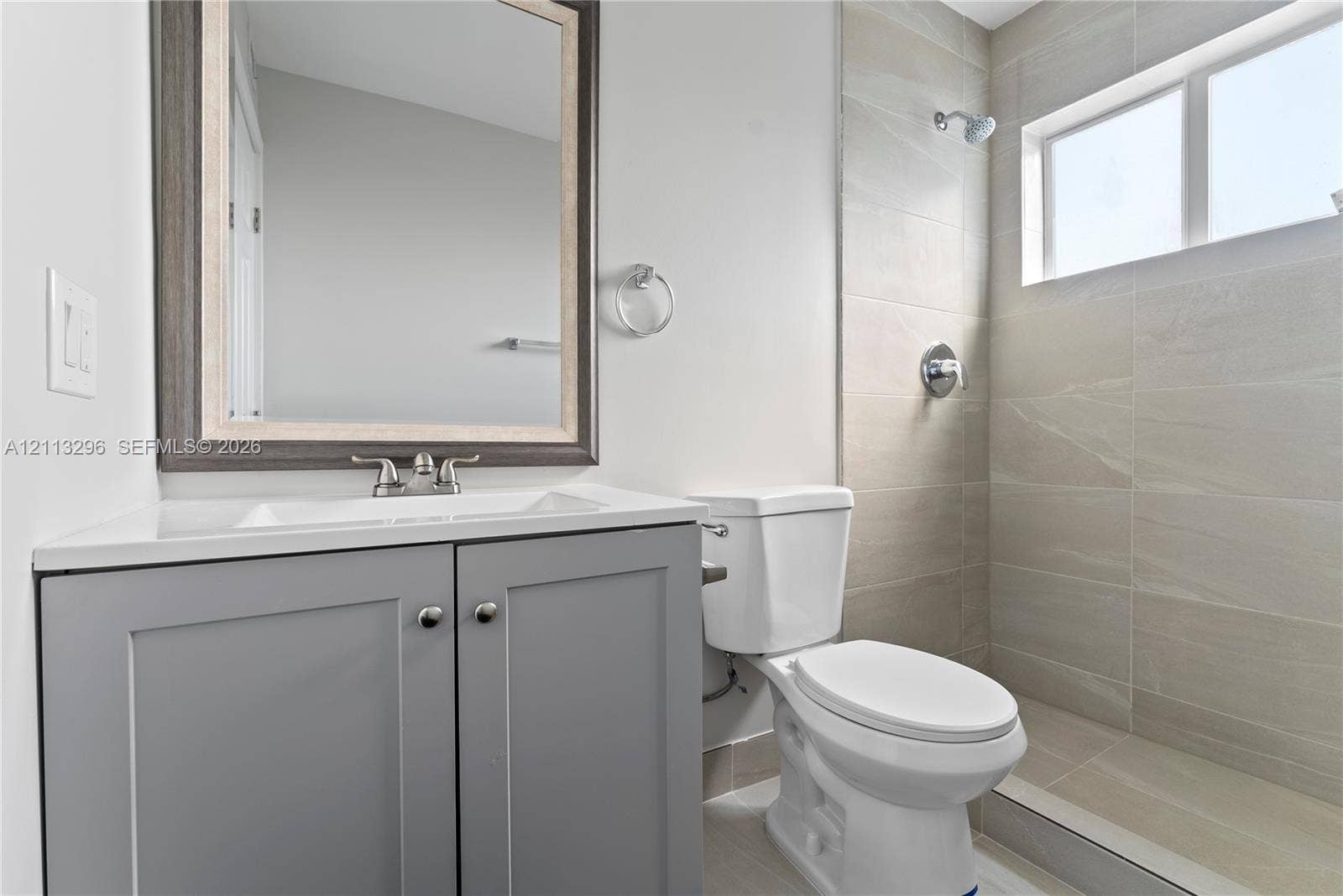 1101 NE 80th Street, #302, Miami, Miami, FL 33138 Bathroom featuring a gray shaker-style vanity with an integrated sink, framed wall-mounted mirror, ceramic tile shower surround, and a horizontal window