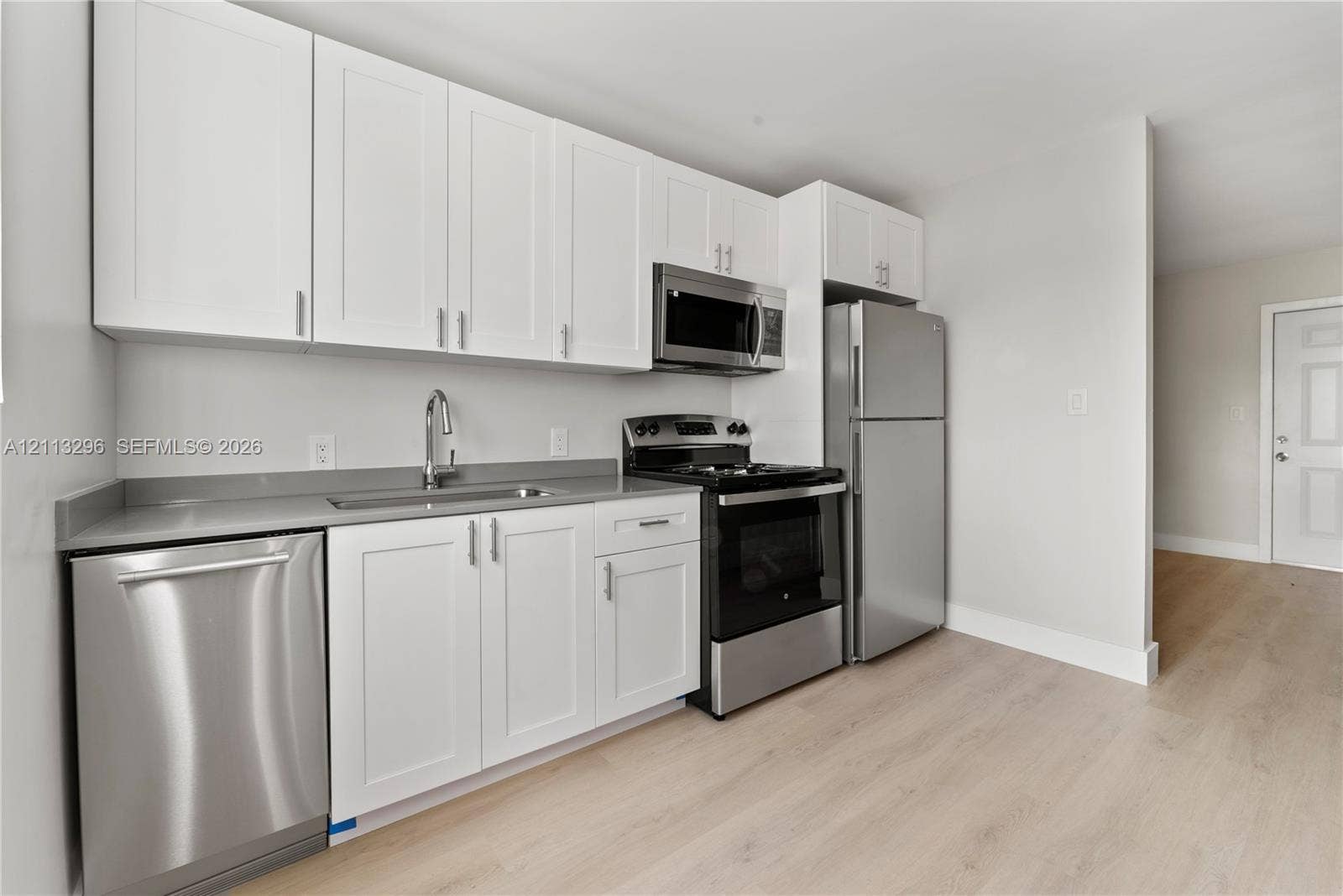 1101 NE 80th Street, #302, Miami, Miami, FL 33138 Kitchen featuring white shaker-style cabinetry, grey solid-surface countertops, wood-finish flooring, and a stainless steel appliance package including a dishwasher, microwave, range, and refrigerator