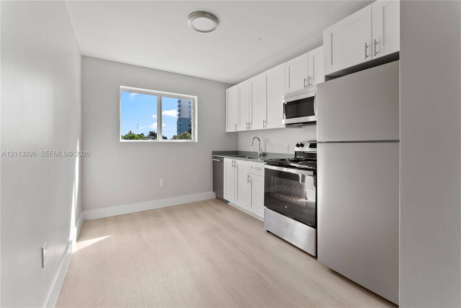 1101 NE 80th Street, #302, Miami, Miami, FL 33138 Kitchen featuring white shaker-style cabinetry, stainless steel appliances, a single-basin sink, and wood-finish flooring