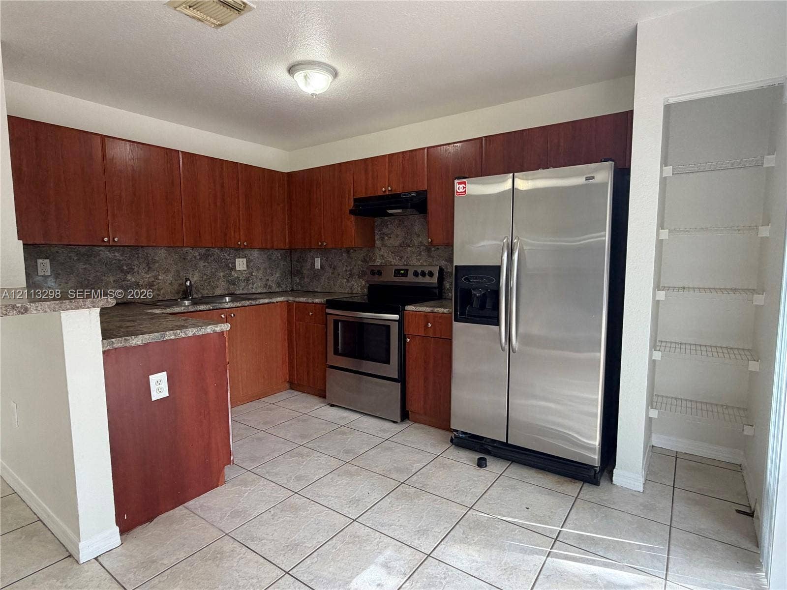 Kitchen featuring wood-tone cabinetry, stainless steel appliances, a tile backsplash, tile flooring, and a walk-in pantry with wire shelving