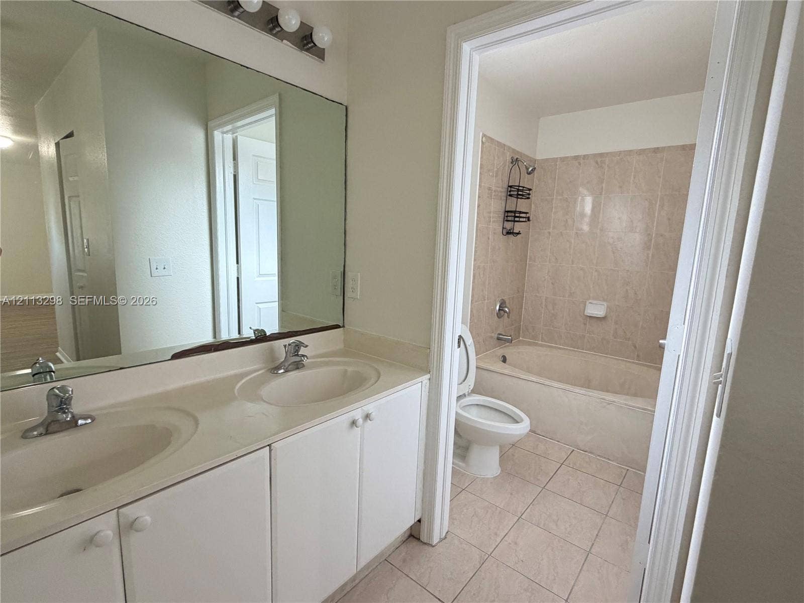 Dual-basin vanity with integrated sinks, large wall-mounted mirror, light-tone cabinetry, tiled flooring, and a combined tub and shower enclosure with wall-mounted ceramic tile surround