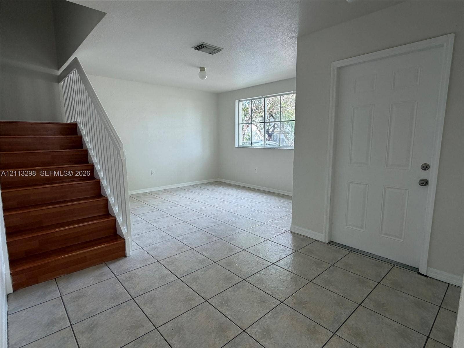 Neutral-toned tile flooring, staircase with wood-finish treads, white metal handrail, and multi-panel entry door