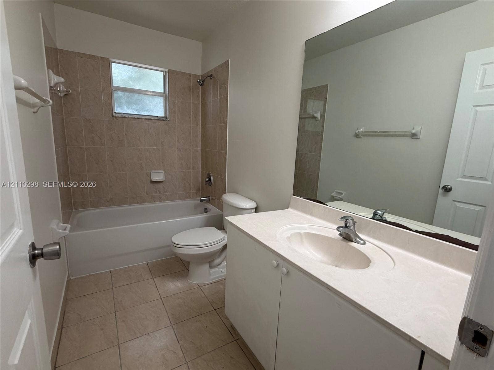 Bathroom featuring a vanity with a solid-surface countertop, an integrated sink, full-width mirror, tile flooring, and a tiled shower-tub enclosure