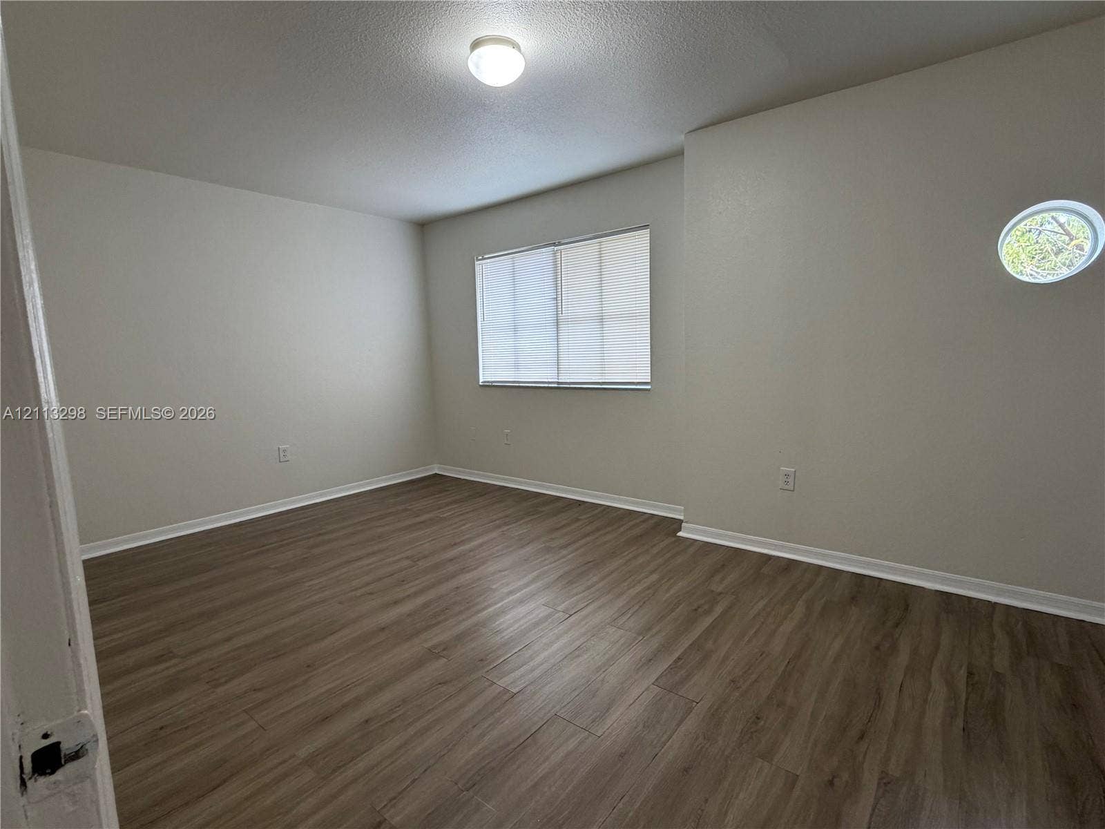 Interior room featuring wood-finish flooring, a rectangular window with integrated blinds, a circular accent window, and a ceiling-mounted light fixture